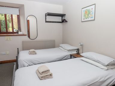 A bedroom with two single beds side by side a small bedside table a wall-mounted coat rack and a window at Brimpts Barn Dartmeet near Princetown