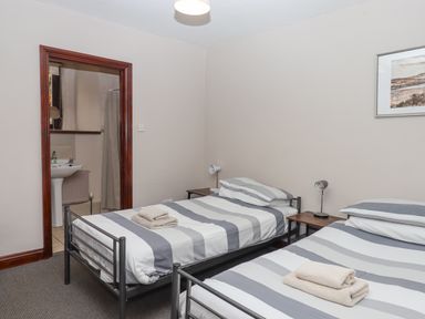 A bedroom with two single beds and towels on them near a door to a bathroom at Brimpts Barn in Dartmeet near Princetown
