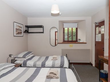 A bedroom with two single beds with striped bedding a window a radiator a wooden door and a wall mirror at Brimpts Barn Dartmeet near Princetown
