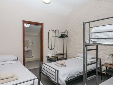 A bedroom with metal frame beds a small wooden side table a wall mirror and an open door leading to a bathroom at Brimpts Barn in Dartmeet near Princetown