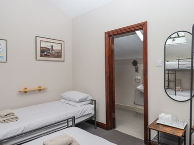 A bedroom with two single beds a wooden door leading to a bathroom and a mirror reflecting a bunk bed at Brimpts Barn in Dartmeet near Princetown