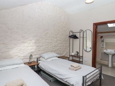 A bedroom with two single beds two bedside tables a lamp a clothes rack with hangers a mirror and an open door to a bathroom at Brimpts Barn Dartmeet near Princetown