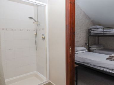 A shower area with a handheld showerhead and a tiled wall next to a bedroom with bunk beds at Brimpts Barn Dartmeet near Princetown