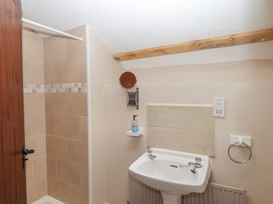 A bathroom with a tiled shower area a white sink a small wall-mounted mirror and a wooden ceiling beam at Brimpts Barn Dartmeet near Princetown