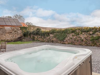 An outdoor hot tub with gravel ground and a stone wall with ivy at Brimpts Barn Dartmeet near Princetown
