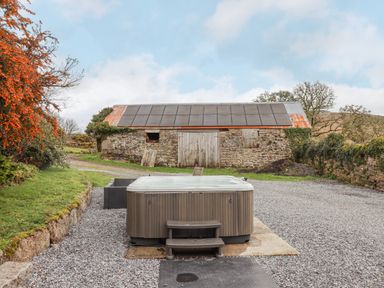 An outdoor hot tub on gravel with a stone barn and solar panels in the background at Brimpts Barn Dartmeet near Princetown