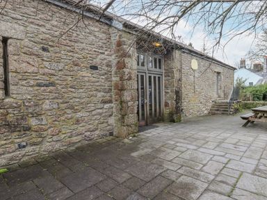 An outdoor stone patio area with a large wooden door set in a stone wall stairs leading to a side entrance and a wooden picnic bench at Brimpts Barn Dartmeet near Princetown