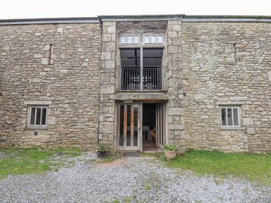 Stone facade of a building with two small windows and a large glass door with balcony above at Brimpts Barn Dartmeet near Princetown