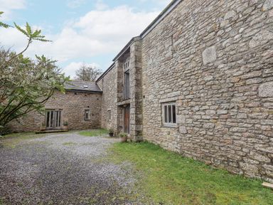 The exterior of a stone barn with gravel and grass courtyard at Brimpts Barn Dartmeet near Princetown