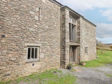 The exterior of a stone building with small windows a glass door with a balcony above and two flowerpots on the ground at Brimpts Barn in Dartmeet near Princetown