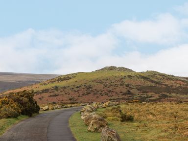 A winding road bordered by rocks with hills and vegetation under a partly cloudy sky at Brimpts Barn Dartmeet near Princetown