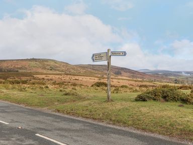 A road sign at a rural intersection with hills and shrubs in the background at Brimpts Barn in Dartmeet near Princetown