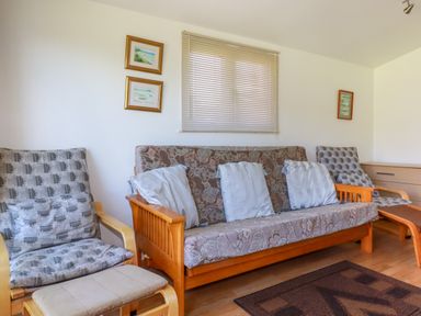 A living room with wooden framed seating and cushions with a window and framed pictures on the wall at Cornish Holiday at Atlantic Bays in St Merryn