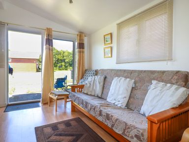 A living room with a sofa bed three cushions paintings on the wall and glass sliding doors at Cornish Holiday at Atlantic Bays in St Merryn