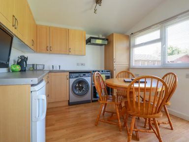 A kitchen with wooden cabinets a round wooden dining table and four chairs next to a large window at Cornish Holiday at Atlantic Bays in St Merryn