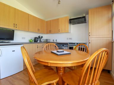 A kitchen with wooden cabinets a round wooden dining table with four chairs and kitchen appliances at Cornish Holiday at Atlantic Bays in St Merryn