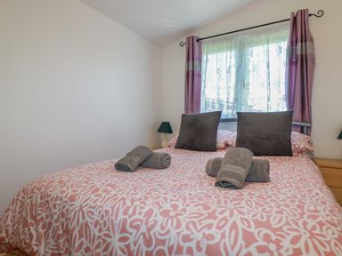 A bedroom with a bed covered in patterned bedding two gray pillows rolled towels on the bed and a window with curtains at Cornish Holiday at Atlantic Bays in St Merryn