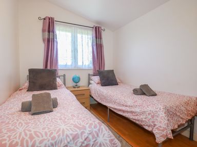 A bedroom with two single beds bedside table and window with curtains at Cornish Holiday at Atlantic Bays in St Merryn