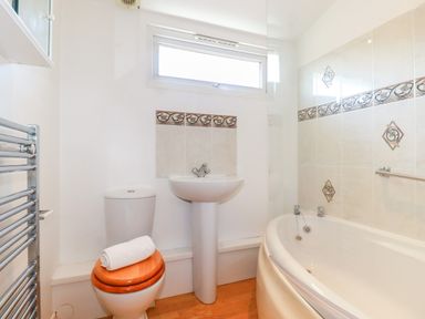 A bathroom with a toilet with wooden seat and rolled towel sink and bathtub with tiled walls at Cornish Holiday at Atlantic Bays in St Merryn