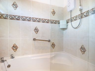 A bathroom with a bathtub shower unit and decorative tiled walls at Cornish Holiday at Atlantic Bays in St Merryn