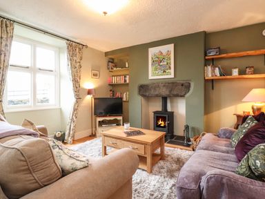 A living room with sofas a wooden coffee table a fireplace a television and bookshelves at Lavender Cottage in Coniston
