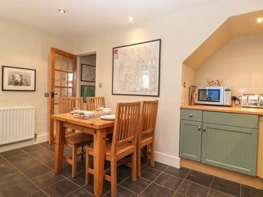 A dining area with wooden table and chairs next to a kitchen counter with microwave and toaster at Lavender Cottage in Coniston