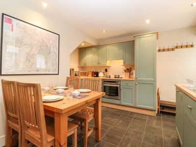 A kitchen with green cabinets wooden dining table with four chairs and a large framed map on the wall at Lavender Cottage in Coniston