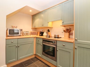 A kitchen with green cabinets a microwave toaster oven utensils and a stove at Lavender Cottage in Coniston