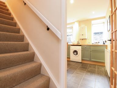 A carpeted staircase next to a kitchen with green cabinets a washing machine and two windows at Lavender Cottage in Coniston
