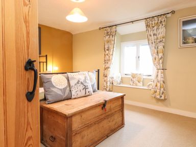 A bedroom with a wooden chest at the foot of the bed and a window seat with cushions at Lavender Cottage in Coniston