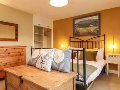A bedroom with a bed pillows a wooden chest a dresser a mirror an open closet and a painting on the wall at Lavender Cottage Coniston