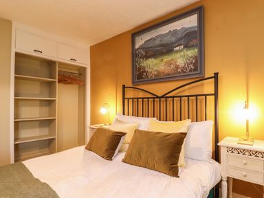 A bedroom with a bed and pillows open closet shelves and bedside tables with lamps at Lavender Cottage in Coniston
