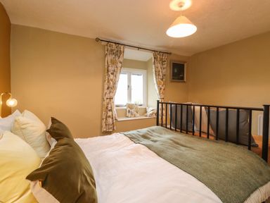 A bedroom with a bed pillows window with curtains and cushions and a picture on the wall at Lavender Cottage in Coniston