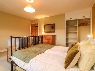 A bedroom with a bed pillows a wooden chest a chest of drawers mirror and an open wardrobe at Lavender Cottage in Coniston