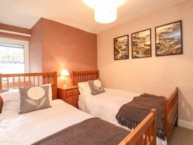 A bedroom with two single wooden beds with white bedding and gray cushions a bedside table with a lamp and three framed pictures on the wall at Lavender Cottage in Coniston