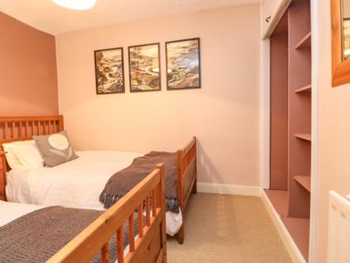 A bedroom with two single wooden beds gray blankets and three framed pictures on the wall at Lavender Cottage in Coniston