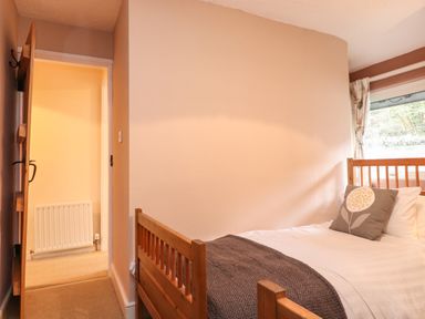 A bedroom with a wooden bed a pillow and a blanket near a window and an open door showing a radiator at Lavender Cottage in Coniston