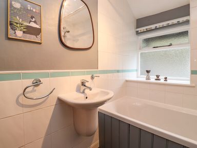 A bathroom with a sink and bathtub next to a window with three figurines on the windowsill at Lavender Cottage in Coniston