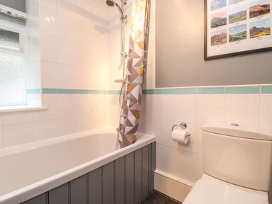A bathroom with a bathtub with shower curtain a toilet and a window at Lavender Cottage in Coniston