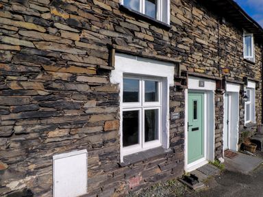 A stone cottage exterior with white framed windows and a green door at Lavender Cottage in Coniston