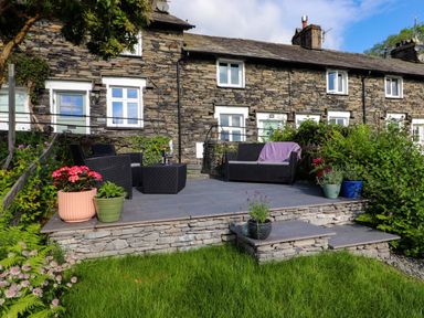 An outdoor seating area with black wicker furniture and potted plants in front of a stone house at Lavender Cottage in Coniston