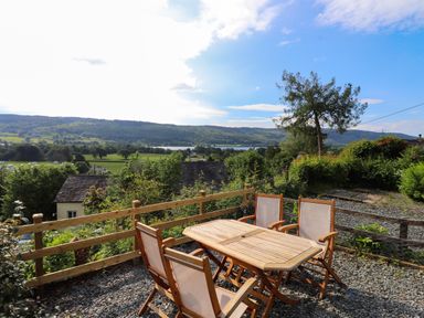 An outdoor seating area with a wooden table and four chairs overlooking green fields trees and hills at Lavender Cottage in Coniston