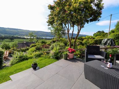 A garden patio with plants and outdoor furniture overlooking fields and hills at Lavender Cottage in Coniston