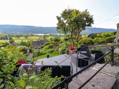 An outdoor patio with black wicker chairs and a table overlooking a garden and distant hills at Lavender Cottage in Coniston