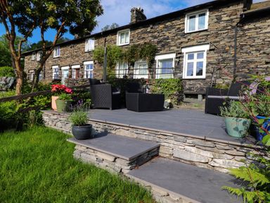 A stone patio with outdoor chairs and potted plants outside a stone house at Lavender Cottage in Coniston