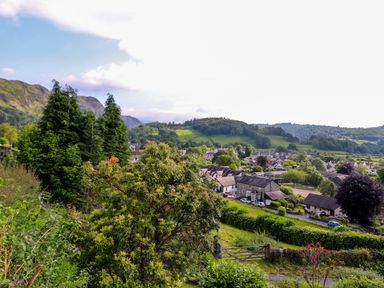 A village with houses surrounded by green hills and trees at Lavender Cottage in Coniston