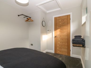 A bedroom with a wooden door a small mirror folded towels on a shelf and a clothes rack with hangers at Ty Bara in Cemaes Bay