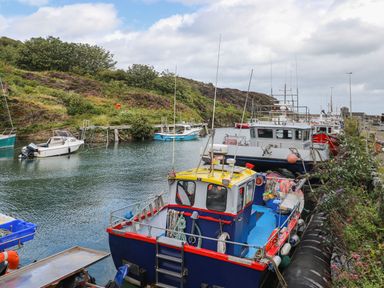 A harbor with fishing boats docked along the quay and a hillside in the background at Ty Bara in Cemaes Bay