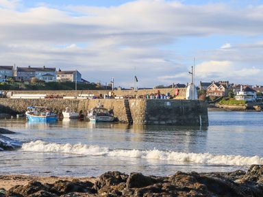 A small harbor with boats docked near a stone pier and houses in the background at Ty Bara in Cemaes Bay