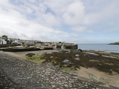 A coastal village with boats docked near a stone pier and houses in the background at Ty Bara in Cemaes Bay